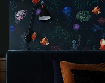 May include: A bedroom wall with a dark blue backdrop, adorned with a vibrant underwater design of jellyfish, fish, and seahorses. A black lamp is mounted above a dark blue headboard. Cushions in brown and black tones are arranged on the bed.
