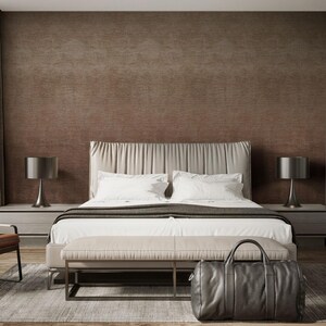May include: A modern bedroom with a large bed featuring a cream-colored headboard and white bedding. A gray leather duffel bag sits at the foot of the bed. Two bedside lamps flank the bed, and a bench is placed at the foot of the bed.