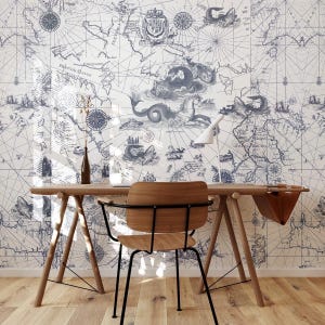 Può includere: Un ufficio domestico con una scrivania e una sedia in legno contro una parete ricoperta da una carta da parati con mappa vintage. La mappa presenta illustrazioni nautiche e una rosa dei venti nei toni del blu e del bianco. Una lampada da scrivania e un vaso sono sulla scrivania.