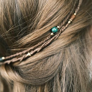 Könnte beinhalten: Nahaufnahme von braunem Haar mit einem geflochtenen Stirnband. Das Stirnband hat kleine goldene Perlen und eine türkisfarbene Perle. Das Haar ist hellbraun und wellig, das Stirnband liegt oben auf.