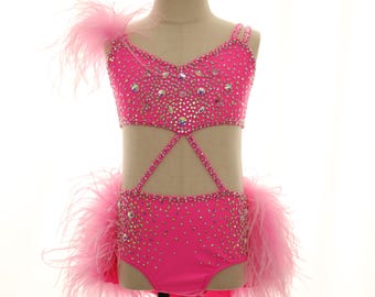 May include: A hot pink dance costume with sparkling rhinestones and feather accents. The two-piece outfit features a cut-out design and is displayed on a mannequin. The costume is designed for dance or performance.