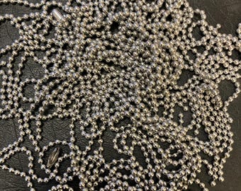 May include: A pile of silver ball chain, a type of chain made of small metal balls connected by links. The chain is on a black surface.