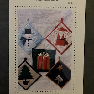 May include: A pattern for paper pieced pot holders with five designs: a snowman, Santa Claus, a gift, a Christmas tree, and a nativity scene. The text on the pattern reads "Paper Pieced Pot Holders" and "...5 paper pieced designs."