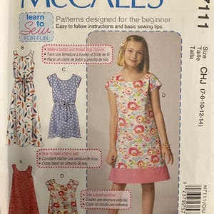 May include: McCall's sewing pattern M7111 for girls' dresses. The pattern includes multiple dress designs with various features, including a fabric belt and faced neckline. The size range is CHJ (7-8-10-12-14).
