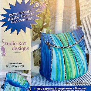 May include: The Uptown Saddlebag pattern by Studio Kat Designs. The bag features a blue, green, and white striped design. Dimensions are 8"L x 6"W x 9"H. Includes a zippered fold-over flap and two separate storage areas.