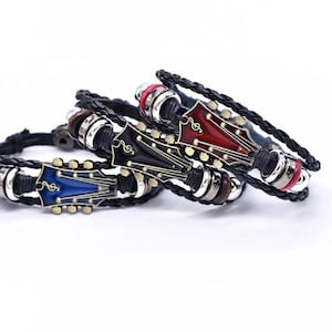 Peut inclure: Trois bracelets en cuir avec des motifs de tête de guitare bleus, noirs et rouges. Chaque bracelet présente une bande en cuir tressé noir et des accents argentés. Les motifs de tête de guitare ont des détails de notes de musique.