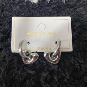 May include: A pair of stainless steel heart-shaped hoop earrings. The earrings are silver and have a polished finish. The earrings are displayed on a white card with the words "Stainless steel" printed on it.