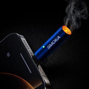 Może przedstawiać: Niebieskie urządzenie z napisem "SMOKA" jest podłączone do smartfona. Urządzenie ma świecący na pomarańczowo koniec, z którego wydobywa się dym. Na urządzeniu widoczne jest również zielone światło. Tło jest czarne.