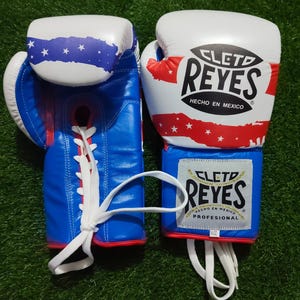 Peut inclure: Une paire de gants de boxe Cleto Reyes de 16 oz avec un motif aux couleurs blanc, bleu et rouge agrémenté d'étoiles. Les gants présentent des lacets blancs, le logo Cleto Reyes sur le poignet et le dos, ainsi que l'inscription Hecho en Mexico.