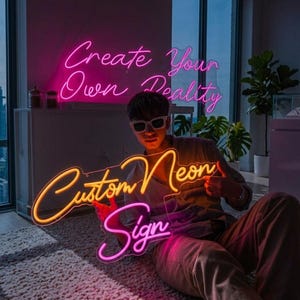 May include: A person holding a custom neon sign with the words "Custom Neon Sign" in pink and yellow. The words "Create Your Own Reality" are in pink neon in the background. The person is wearing sunglasses.