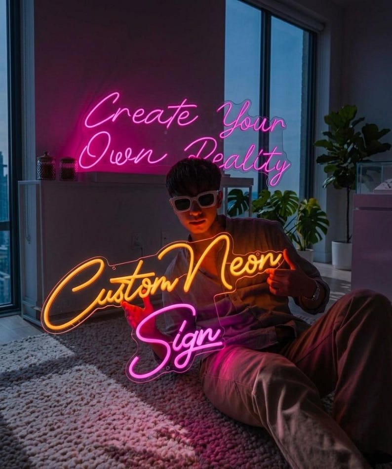 May include: A person holding a custom neon sign with the words "Custom Neon Sign" in pink and yellow. The words "Create Your Own Reality" are in pink neon in the background. The person is wearing sunglasses.