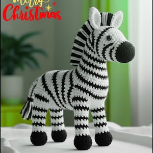 Könnte beinhalten: Ein gehäkeltes Zebra mit schwarz-weißen Streifen, schwarzen Hufen und einer schwarzen Mähne. Der Text "merry Christmas" steht in Rot und Gelb über dem Zebra. Dieser Dekorationsartikel eignet sich für die Weihnachtsdekoration.