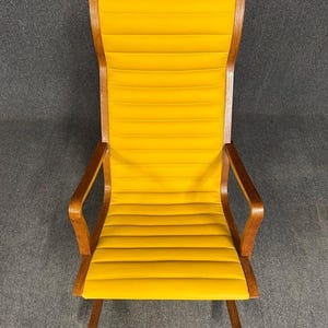 May include: A high-backed, mid-century modern armchair with a bright yellow, horizontally ribbed seat and back. The frame and armrests are made of wood with a warm, natural finish. The chair has a minimalist design.