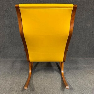 May include: A mid-century modern rocking chair with a bright yellow upholstered back and seat. The chair has a wooden frame with curved rockers and a high back. The chair is a vibrant accent piece.