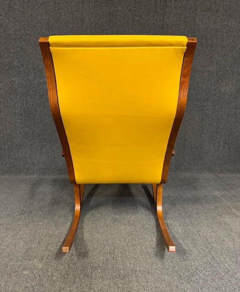 May include: A mid-century modern rocking chair with a bright yellow upholstered back and seat. The chair has a wooden frame with curved rockers and a high back. The chair is a vibrant accent piece.