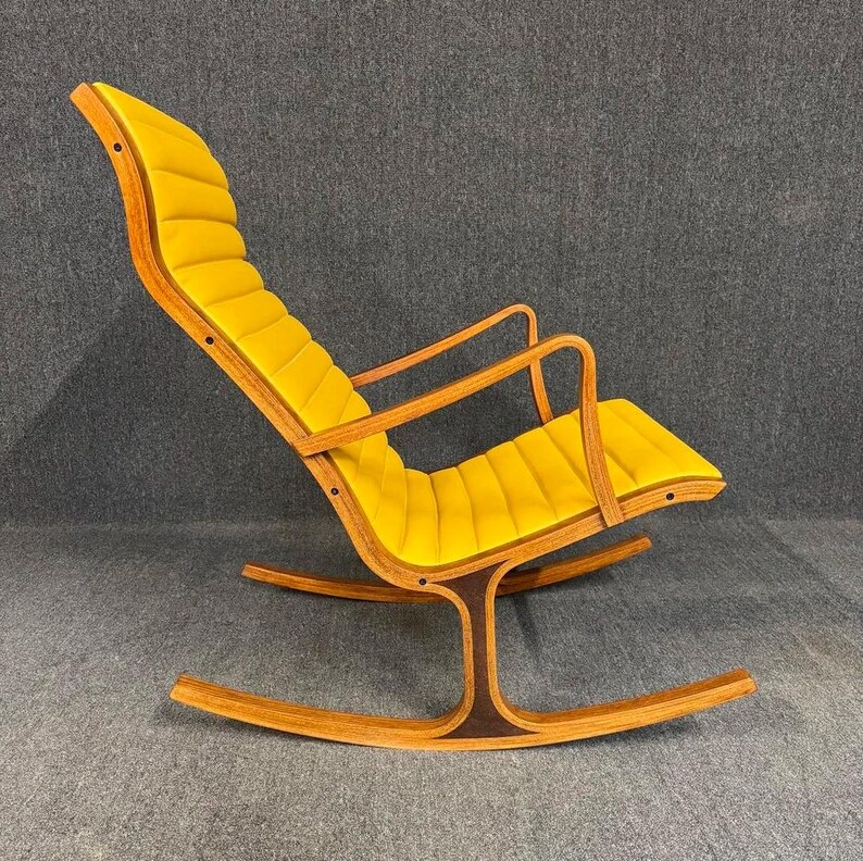 May include: A mid-century modern rocking chair with a yellow cushioned seat and backrest. The chair has a wooden frame with curved rockers and armrests. The design features a unique, curved base and a comfortable, inviting appearance.