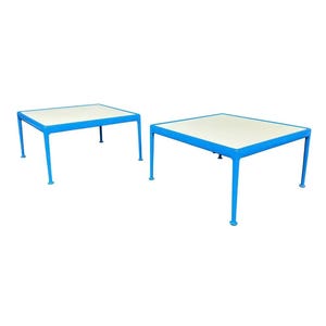 May include: Two square tables with a white top and bright blue legs. The tables have a modern design and are set against a white background. The tables are approximately 24 inches wide and 18 inches tall.