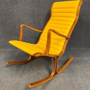 May include: A mid-century modern rocking chair with a bright yellow, padded seat and backrest. The chair features a curved wooden frame and armrests, with a rocking base. The chair's design is simple and elegant, with a focus on comfort and style.