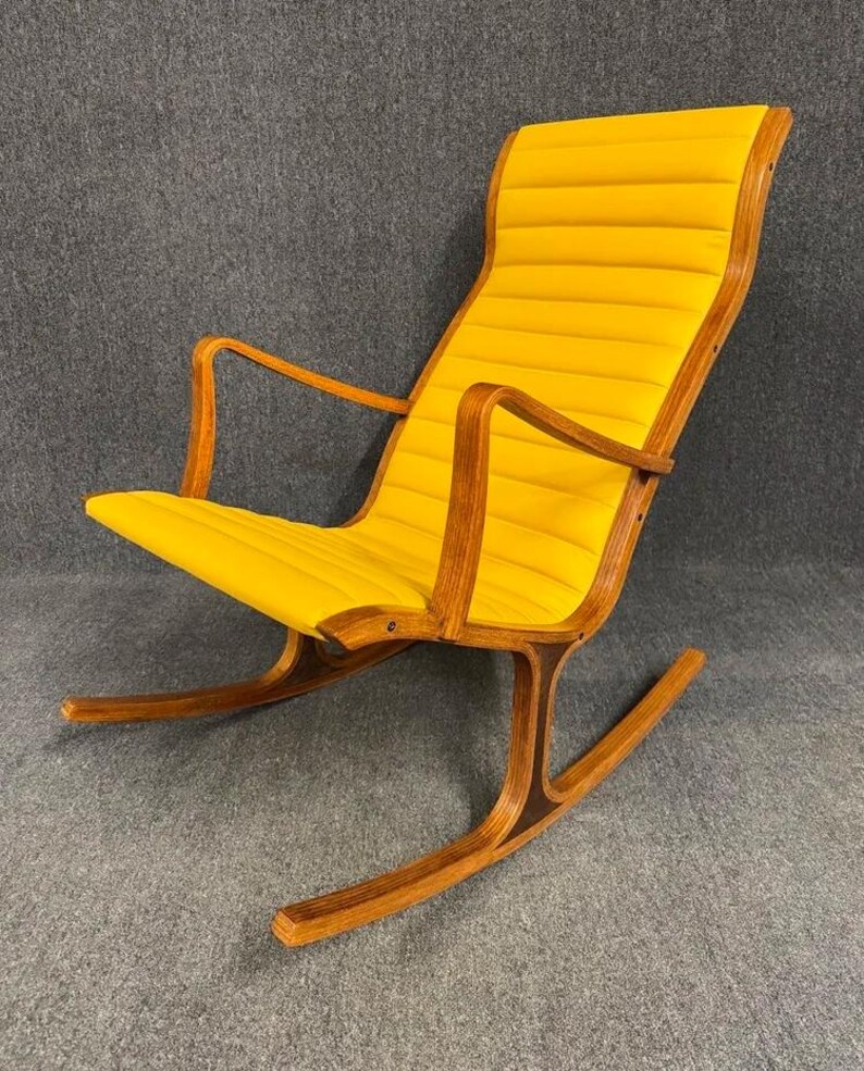 May include: A mid-century modern rocking chair with a bright yellow, padded seat and backrest. The chair features a curved wooden frame and armrests, with a rocking base. The chair's design is simple and elegant, with a focus on comfort and style.