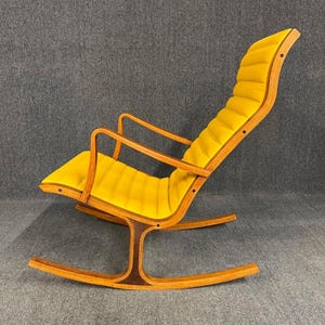 May include: A mid-century modern rocking chair with a bright yellow cushioned seat and backrest. The chair has a curved wooden frame with a dark brown accent on the base. The armrests are also made of wood.