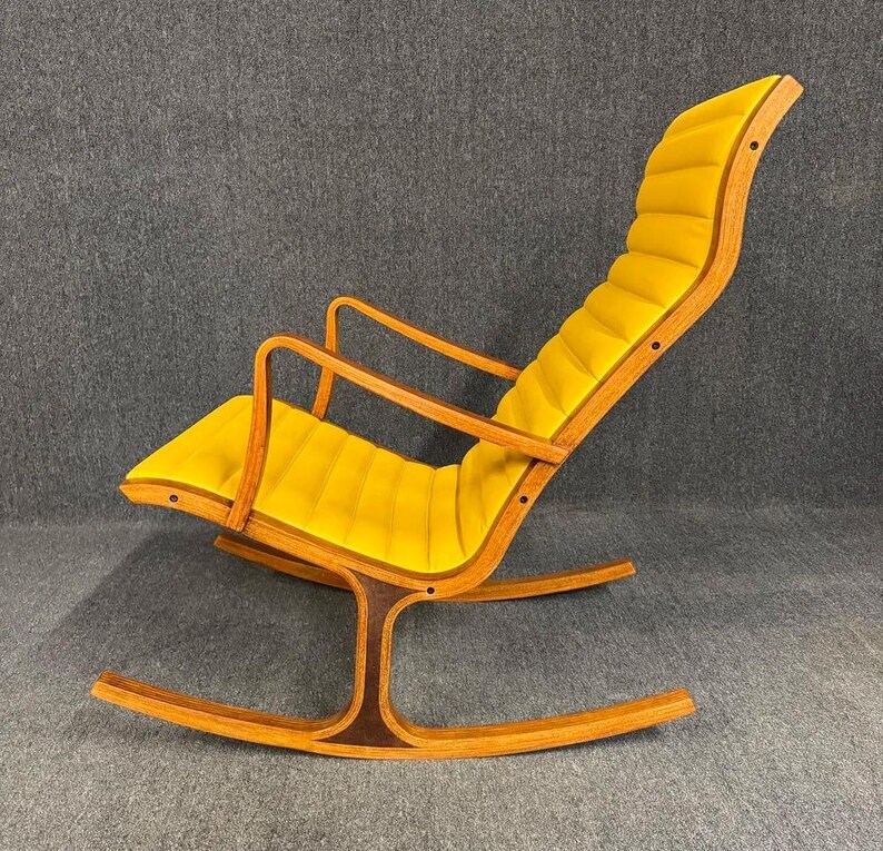 May include: A mid-century modern rocking chair with a bright yellow cushioned seat and backrest. The chair has a curved wooden frame with a dark brown accent on the base. The armrests are also made of wood.