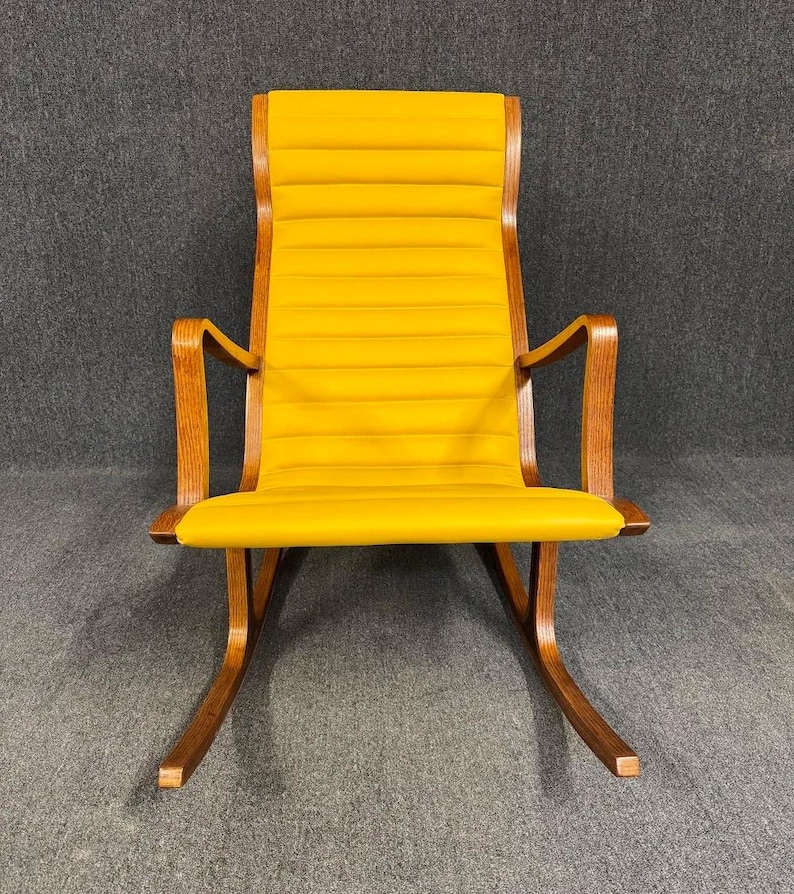May include: A mid-century modern rocking chair with a bright yellow seat and backrest. The chair features a wooden frame with curved armrests and rockers. The seat and back are upholstered with horizontal stitched panels.