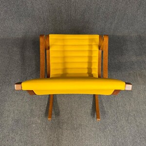 May include: A modern, low-profile chair with a bright yellow seat and backrest. The chair features a wooden frame with a natural finish. The seat and back are made of a ribbed, padded material. The chair is designed for comfort and style.