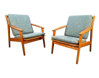 May include: Two mid-century modern armchairs. The chairs have light blue upholstered cushions and wooden frames. The armrests and legs are made of a warm-toned wood. The chairs are set against a white background.