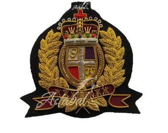 May include: Embroidered patch featuring a detailed crest with a crown, laurel leaves, and a banner. The crest includes a shield with a cross design and the number 9. The patch has gold, red, purple, and black colors.