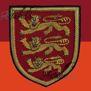 Puede incluir: Parche bordado con un diseño de escudo con fondo rojo y tres leones dorados. El escudo está delineado con ribete dorado y negro. Los leones están detallados con hilo dorado.