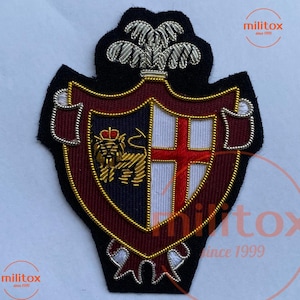 May include: Embroidered patch featuring a shield design with a lion, cross, and crown. The patch has a black border, with red, navy, white, and gold accents. The text "militox since 1999" is visible in the image.