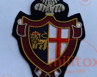 May include: Embroidered patch featuring a shield design with a lion, cross, and crown. The patch has a black border, with red, navy, white, and gold accents. The text "militox since 1999" is visible in the image.