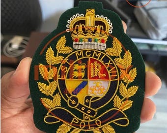Puede incluir: Parche bordado con fondo verde oscuro y detalles dorados y multicolores. El parche presenta una corona, el texto "ST MCMLXVII" y la palabra "POLO". El parche se sostiene en una mano.