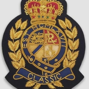 Puede incluir: Parche bordado azul marino con corona dorada, hojas de laurel y un emblema central. El emblema presenta un diseño circular con el texto "MCMXLVII" y la palabra "CLASSIC" en una pancarta azul.