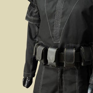 May include: Black tactical jumpsuit with white stitching details. The jumpsuit features a series of small, black leather pouches attached to a belt. The sleeves are long, and the overall design suggests a functional, utilitarian aesthetic.