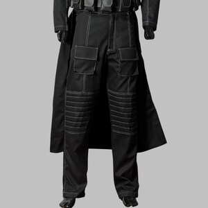 May include: Black pants with white stitching detail, featuring two large pockets on each leg and reinforced knee panels. The pants are part of a black outfit, with a long coat and gloves visible.