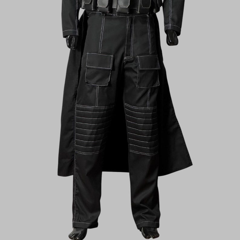May include: Black pants with white stitching detail, featuring two large pockets on each leg and reinforced knee panels. The pants are part of a black outfit, with a long coat and gloves visible.
