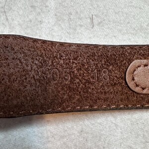 K&ouml;nnte beinhalten: Nahaufnahme eines braunen Lederg&uuml;rtels mit den gepr&auml;gten Zahlen "05 18". Der G&uuml;rtel hat eine strukturierte Oberfl&auml;che und einen gen&auml;hten Rand. Die Schnalle ist auf der rechten Seite sichtbar.