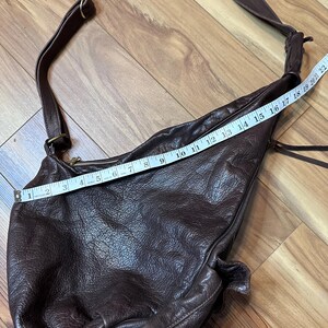 May include: A dark brown leather shoulder bag with a long strap. The bag is measured with a tape measure, showing a length of approximately 22 inches. The leather has a textured appearance.