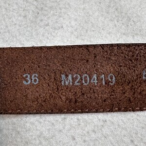 K&ouml;nnte beinhalten: Nahaufnahme eines braunen Lederg&uuml;rtels mit der Gr&ouml;&szlig;e 36. Der G&uuml;rtel hat eine strukturierte Oberfl&auml;che und der Code M20419 ist ebenfalls sichtbar. Der G&uuml;rtel ist wahrscheinlich f&uuml;r Hosen.