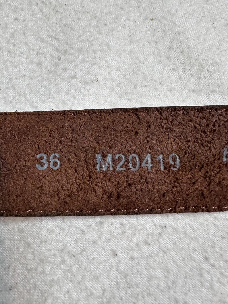 K&ouml;nnte beinhalten: Nahaufnahme eines braunen Lederg&uuml;rtels mit der Gr&ouml;&szlig;e 36. Der G&uuml;rtel hat eine strukturierte Oberfl&auml;che und der Code M20419 ist ebenfalls sichtbar. Der G&uuml;rtel ist wahrscheinlich f&uuml;r Hosen.