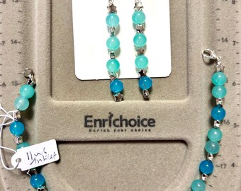 Puede incluir: Un conjunto de joyas con pulsera y pendientes. La pulsera y los pendientes están hechos de cuentas turquesas y azules con detalles de estrellas plateadas. Los pendientes cuelgan de ganchos plateados. El conjunto se exhibe sobre una superficie gris.