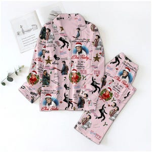 May include: Pink pajama set featuring an Elvis Presley print. The set includes a button-down shirt and matching pants. The design incorporates images of Elvis, text, and Christmas-themed elements.