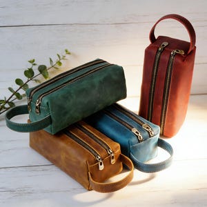 Puede incluir: Cuatro neceseres de cuero en tonos verde, azul, marrón y rojo. Cada bolsa tiene doble cremallera y un asa. Las bolsas rectangulares tienen un asa en un lado. Las cremalleras son plateadas.