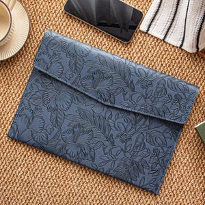 May include: A blue leather laptop sleeve with a floral embossed design. The sleeve has a flap closure and is made of a durable material. The floral pattern includes hibiscus flowers and leaves.
