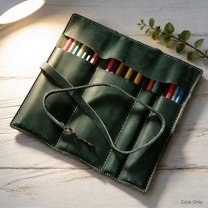 May include: A dark green leather pencil roll case with multiple pockets, holding a variety of colored pencils. The case is secured with a leather strap and buckle. The stitching is white, and the case is on a white wooden surface.