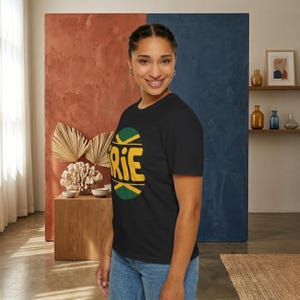Peut inclure: T-shirt noir avec un motif graphique vert, jaune et noir. Le motif présente le mot "RIE" en jaune, avec des accents verts et noirs. Le t-shirt est fait d'une matière douce et convient aux tenues décontractées.