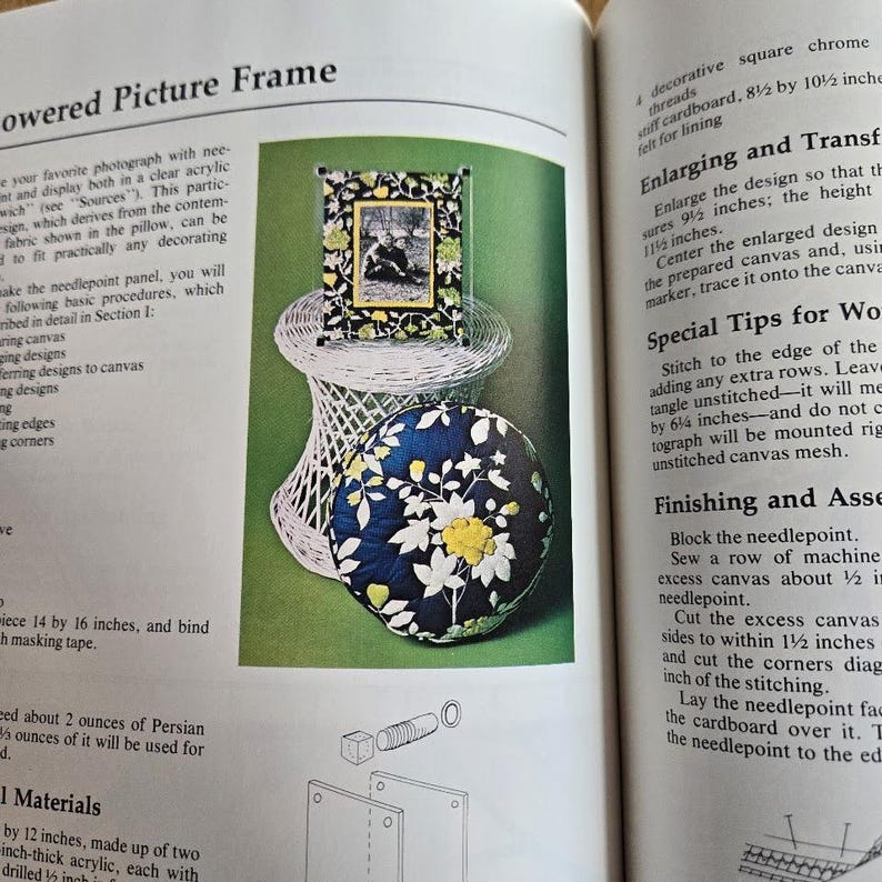 May include: A page from a craft book displays a framed picture on a white wicker stand, and a round cushion with a floral pattern. The frame has a black border with a floral design and a picture inside. The cushion is navy blue with white and yellow flowers.