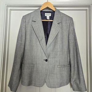May include: A gray blazer with a single black button closure, hanging on a wooden hanger. The blazer has a notched lapel and two front pockets. The interior lining is a dark navy blue. The brand "Pendleton" is visible on the label.