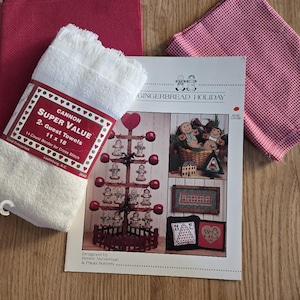 May include: A stack of two white guest towels with a red and white label, a "Gingerbread Holiday" cross-stitch pattern, and two red fabric pieces. The towels are 11 x 18 inches.